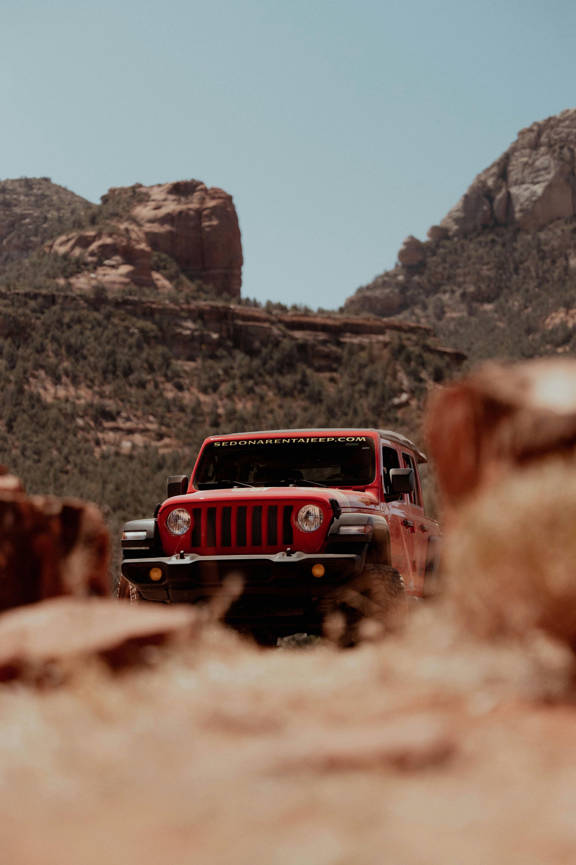 A red jeep is driving down a dirt road in the desert.