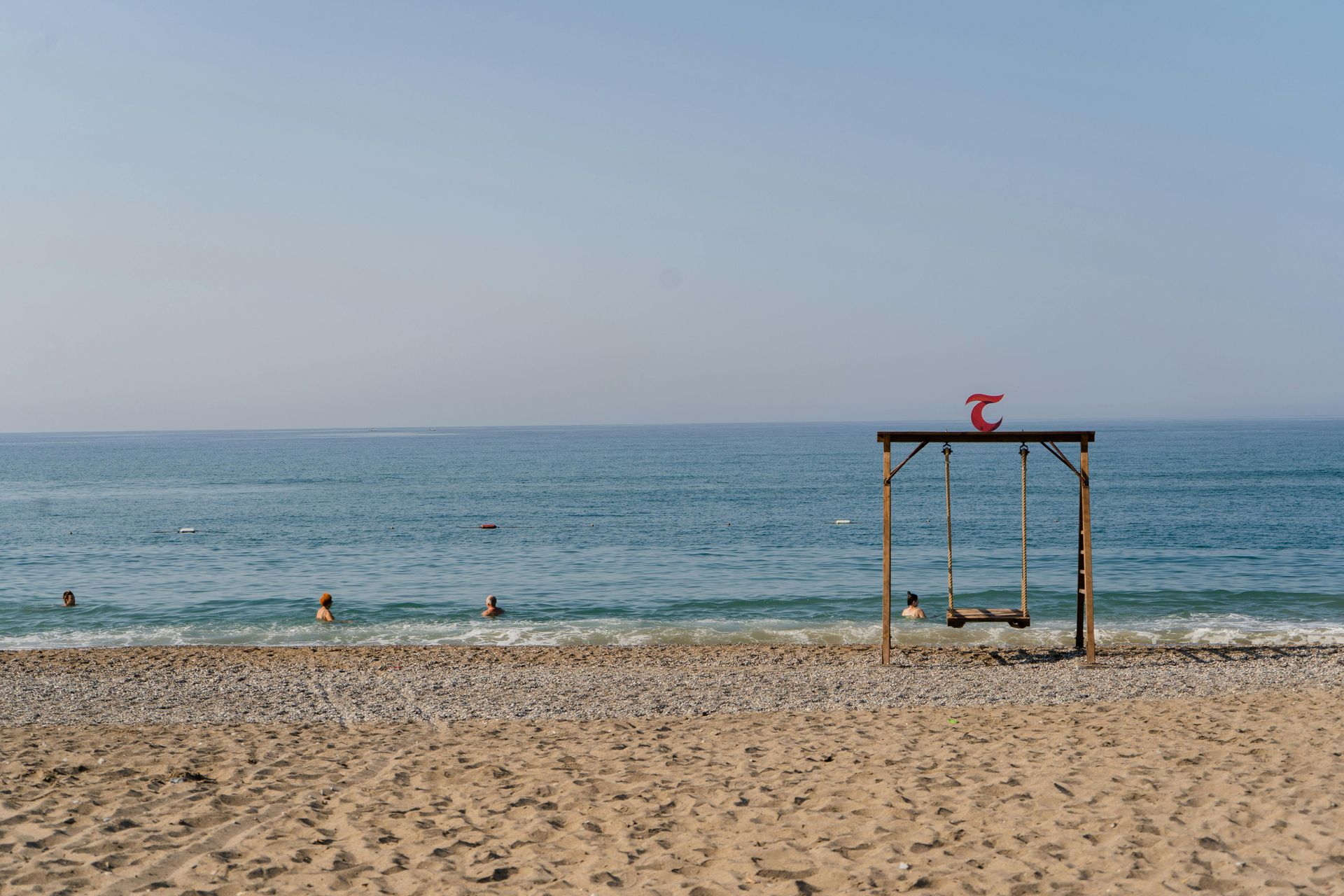 There is a swing on the beach near the ocean.