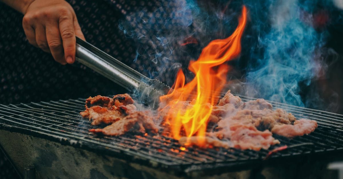 A person is grilling meat on a grill with flames coming out of it.