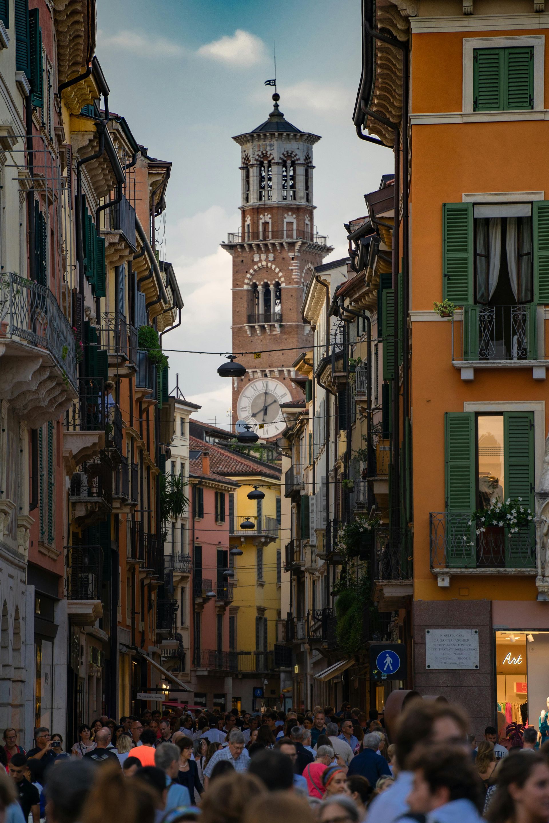 A crowd of people are walking down a narrow street with a clock tower in the background.