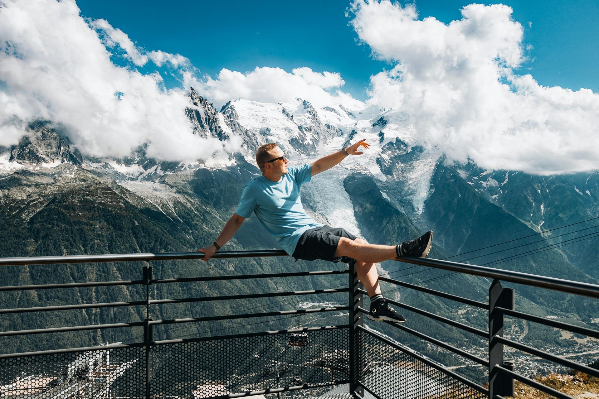 A man is sitting on a railing overlooking a mountain range.