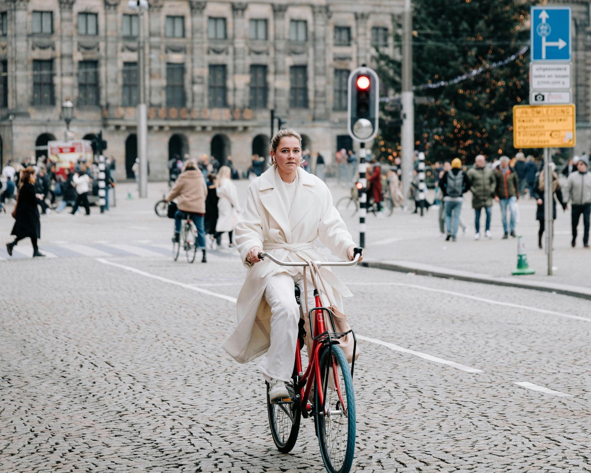 A woman in a white coat is riding a bicycle on a cobblestone street.