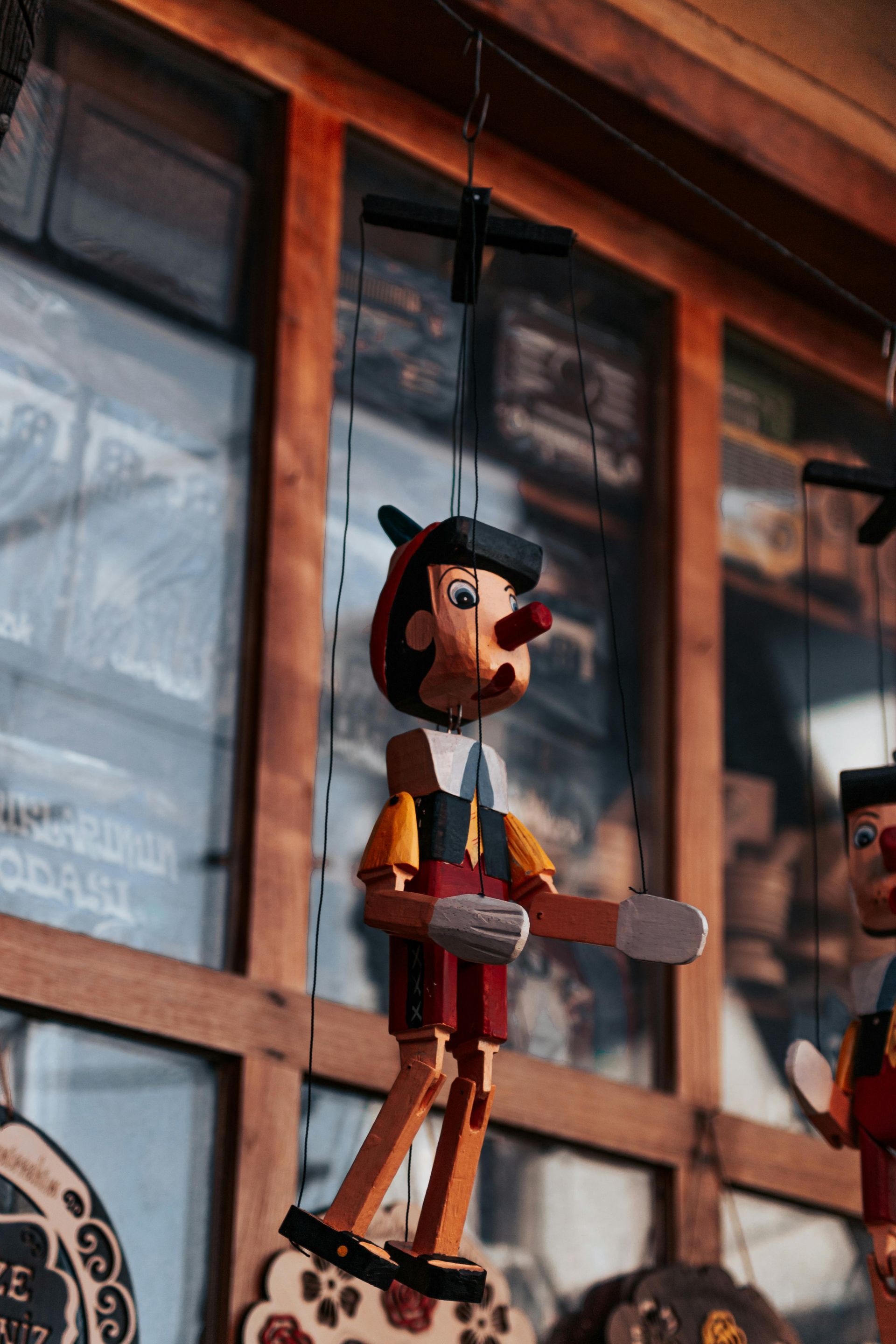 A wooden puppet is hanging from the ceiling in front of a window.