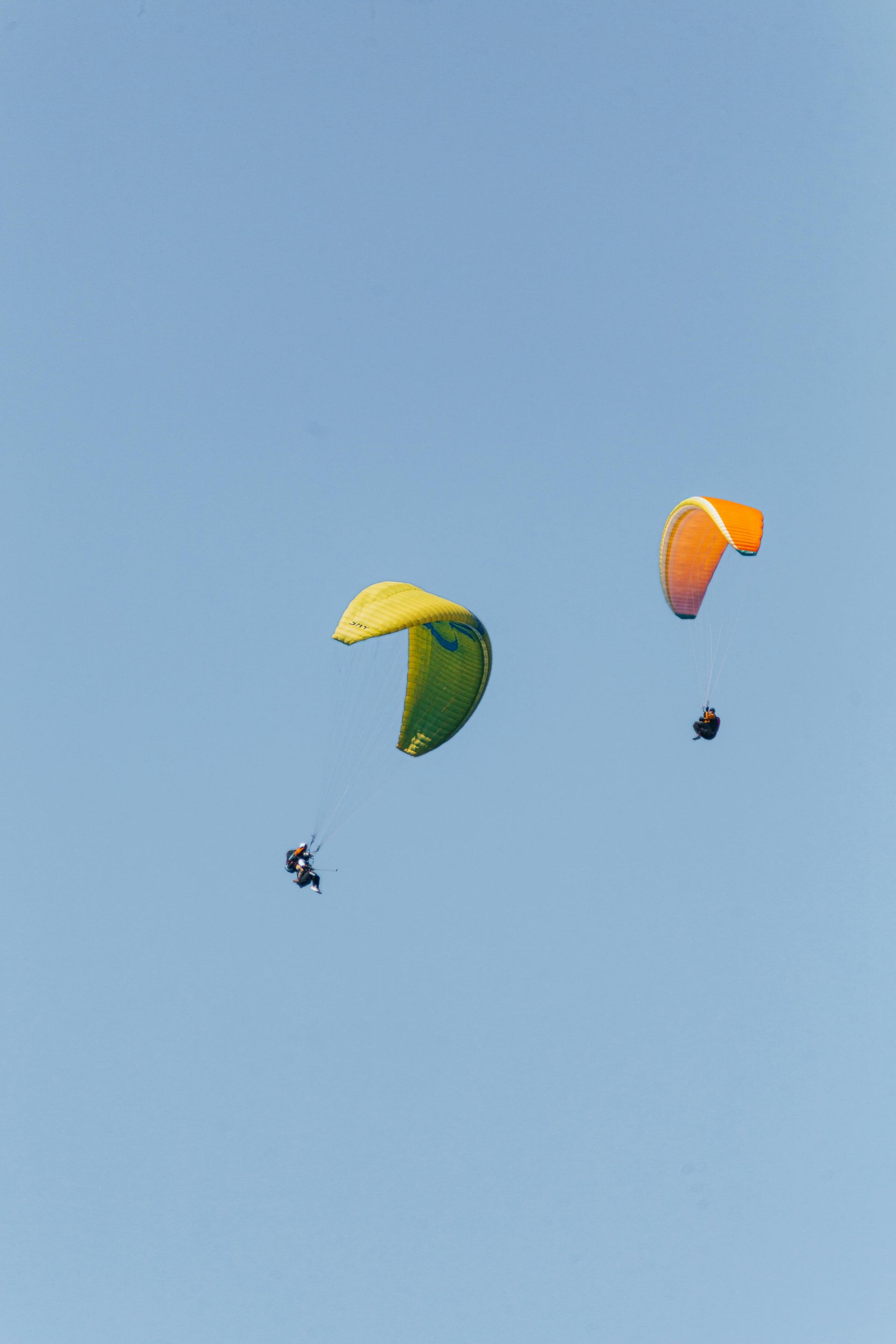 Two people are parasailing in the blue sky.