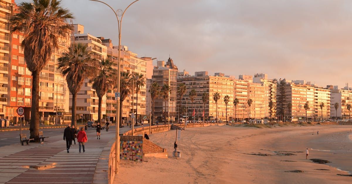 A couple of people are walking down a sidewalk next to a beach.