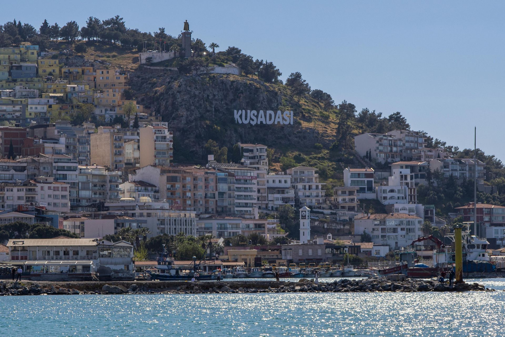 A city with a large sign that says kusadar on top of a hill