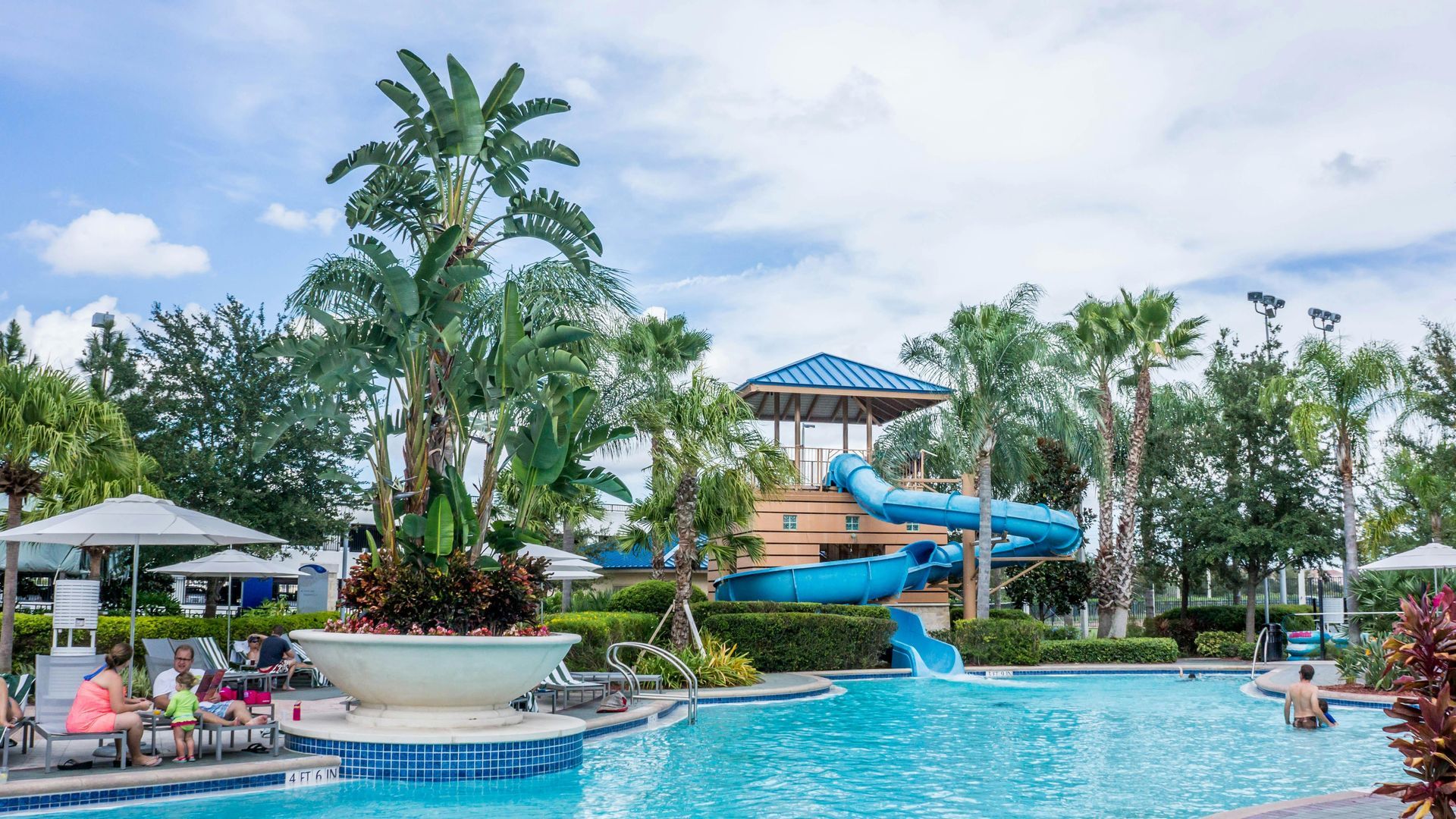 A large swimming pool with a water slide and palm trees in the background.