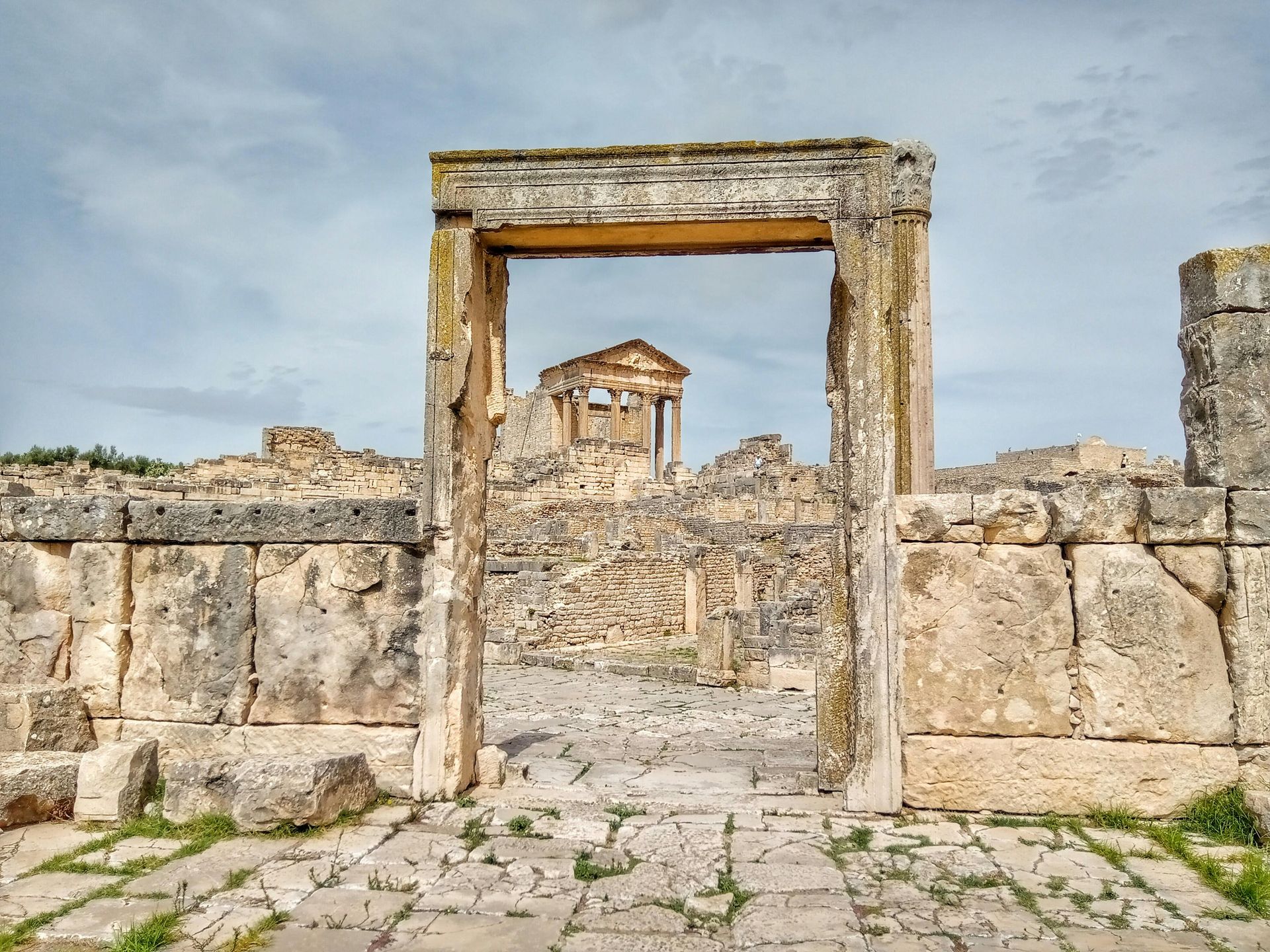 A stone archway leading to a ruined building with a temple in the background.