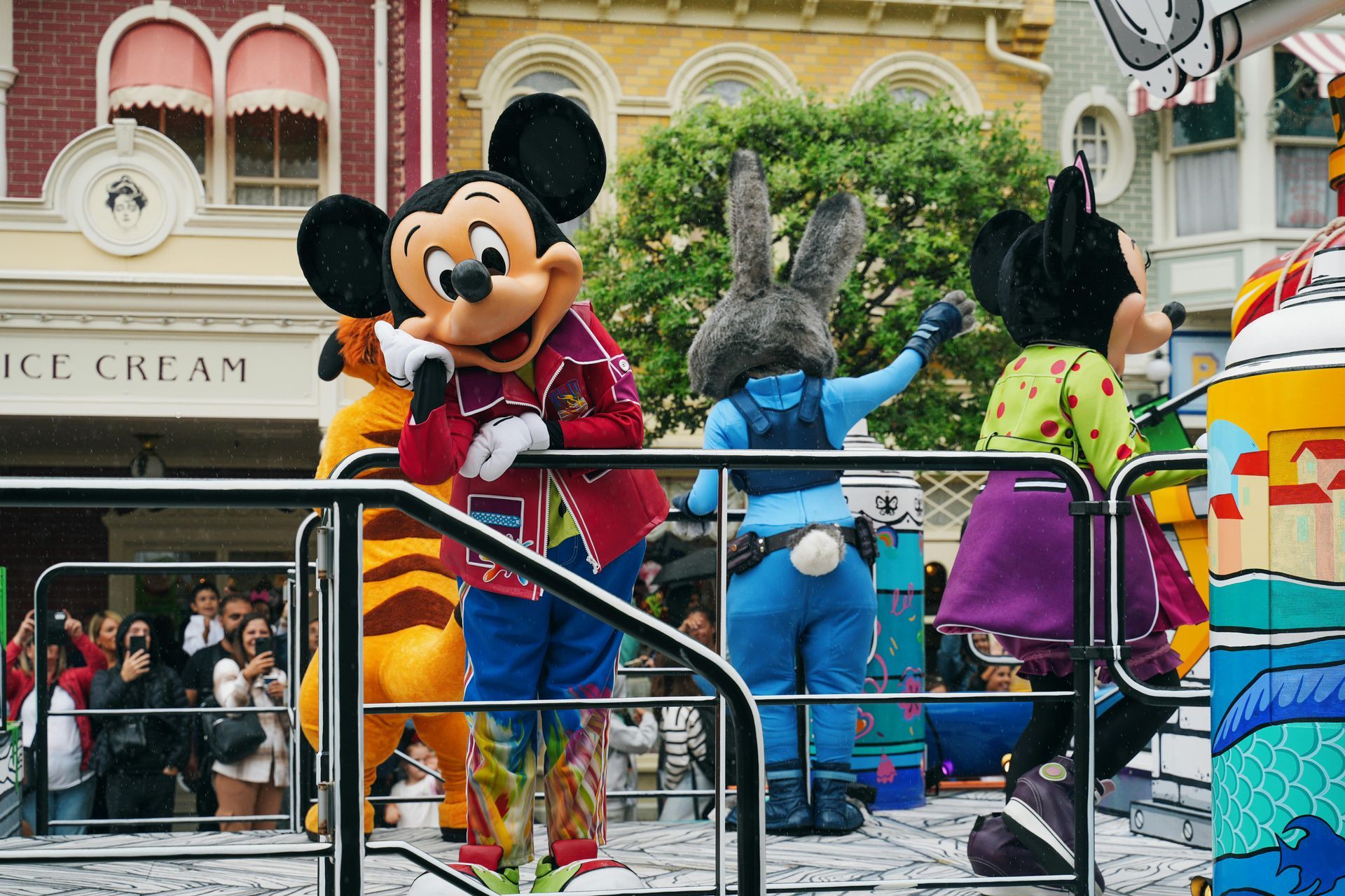 A group of mickey mouse mascots are standing in front of an ice cream shop.