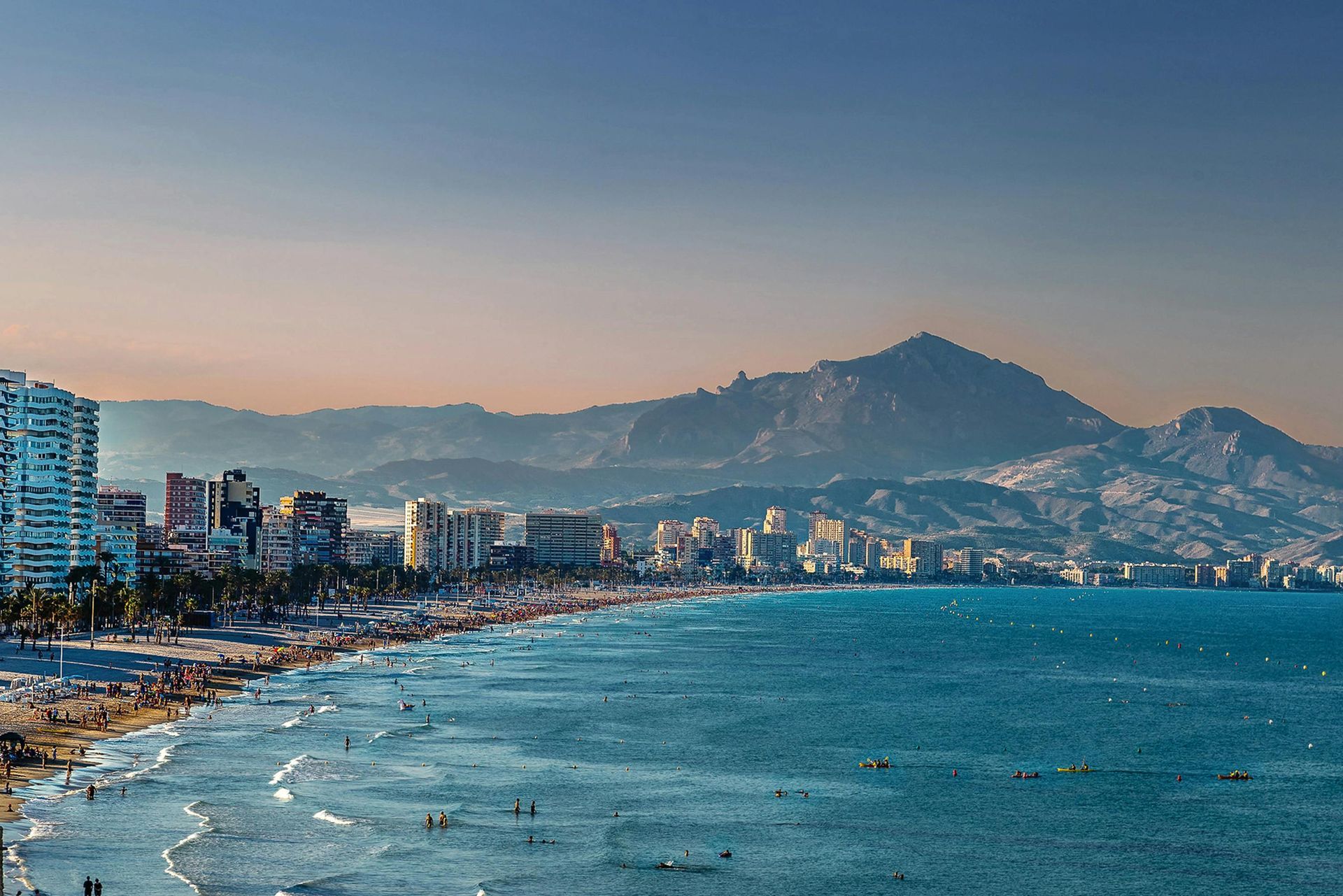 A beach with a city in the background and mountains in the background.