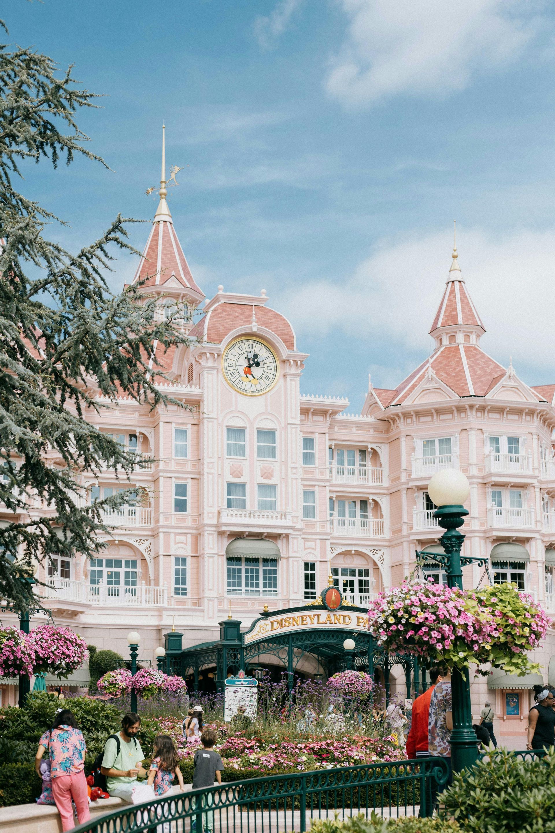 A large pink building with a clock tower and flowers in front of it.