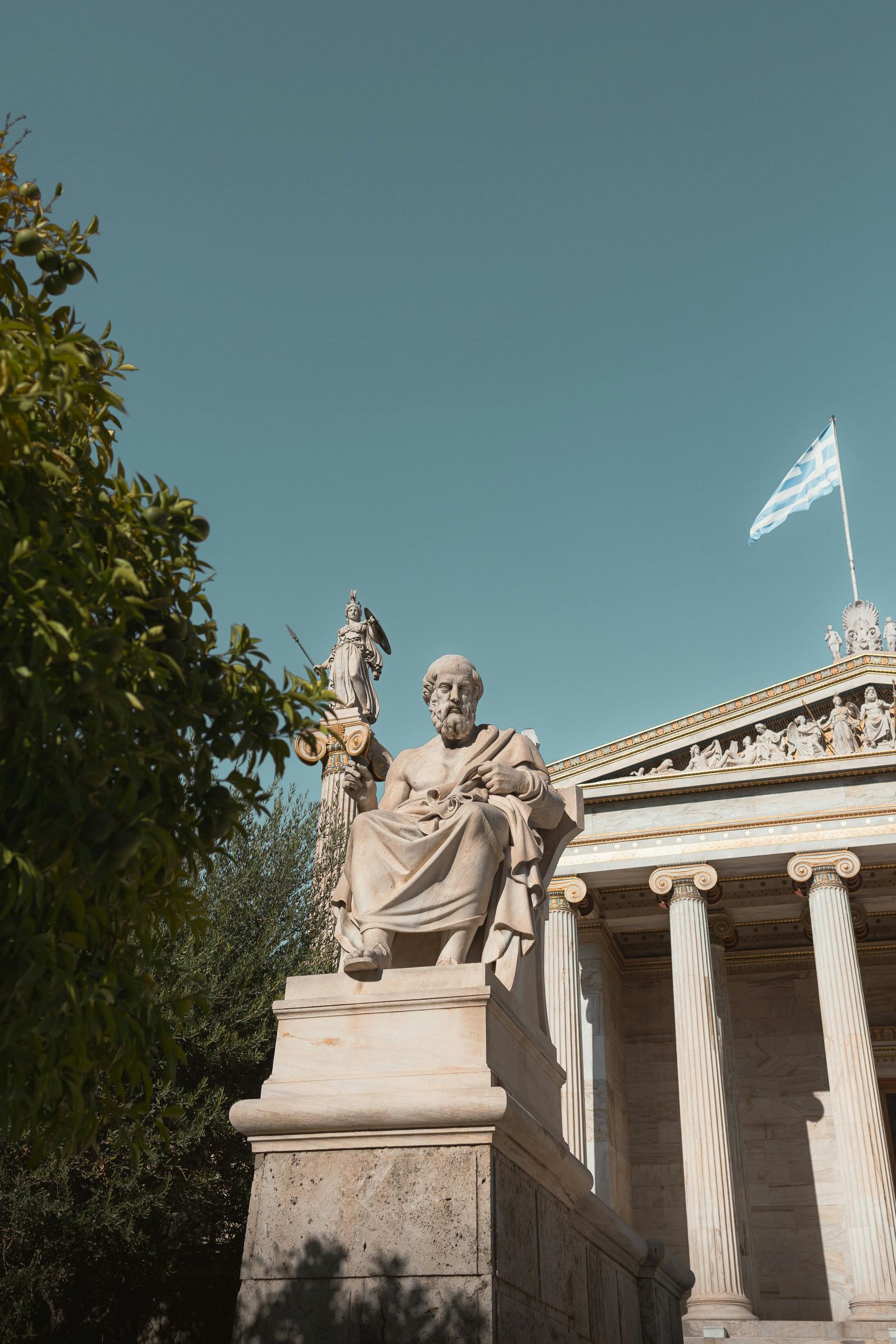 A statue of a man sitting in front of a building with a flag flying in the background.