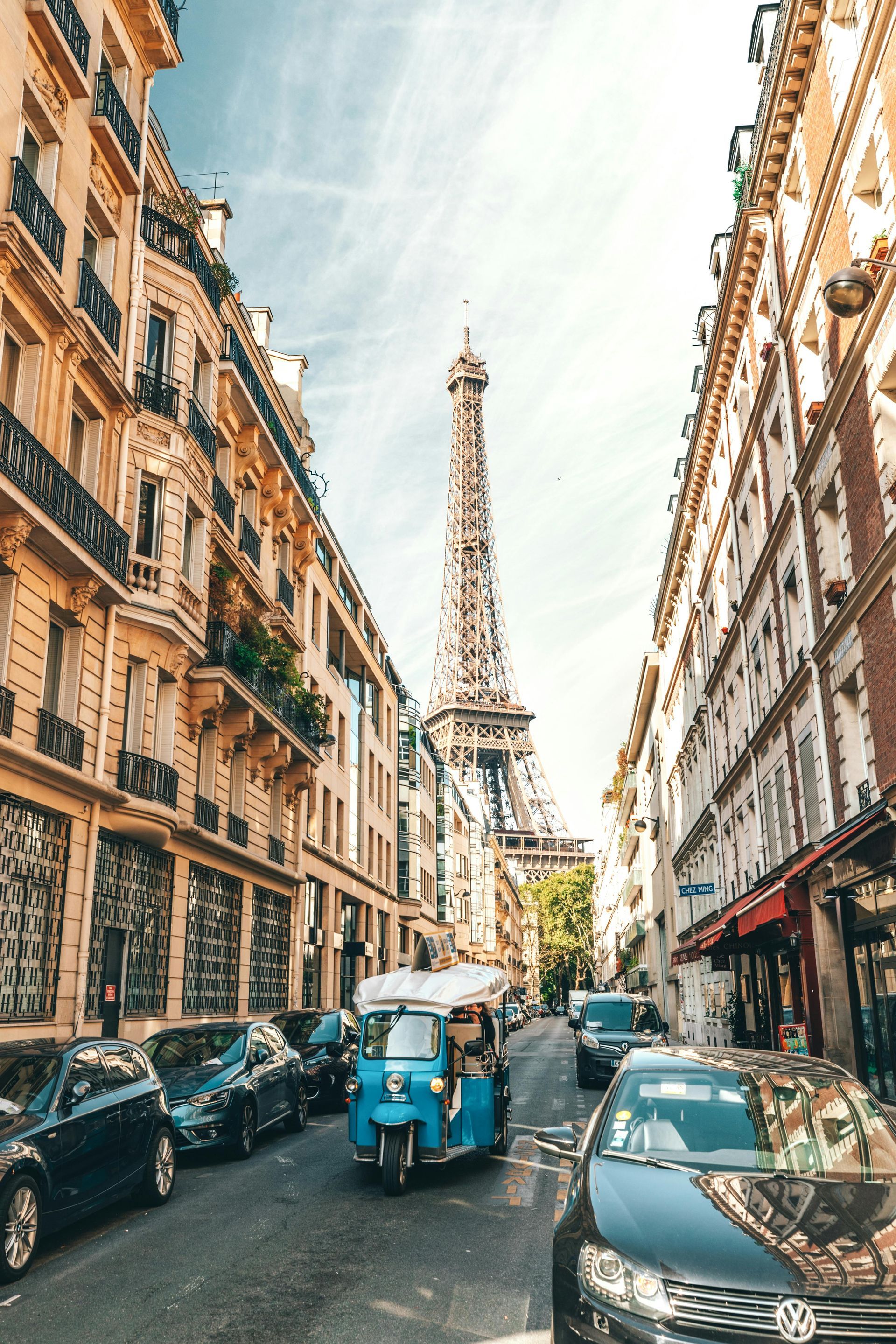 A blue rickshaw is driving down a street in front of the eiffel tower.