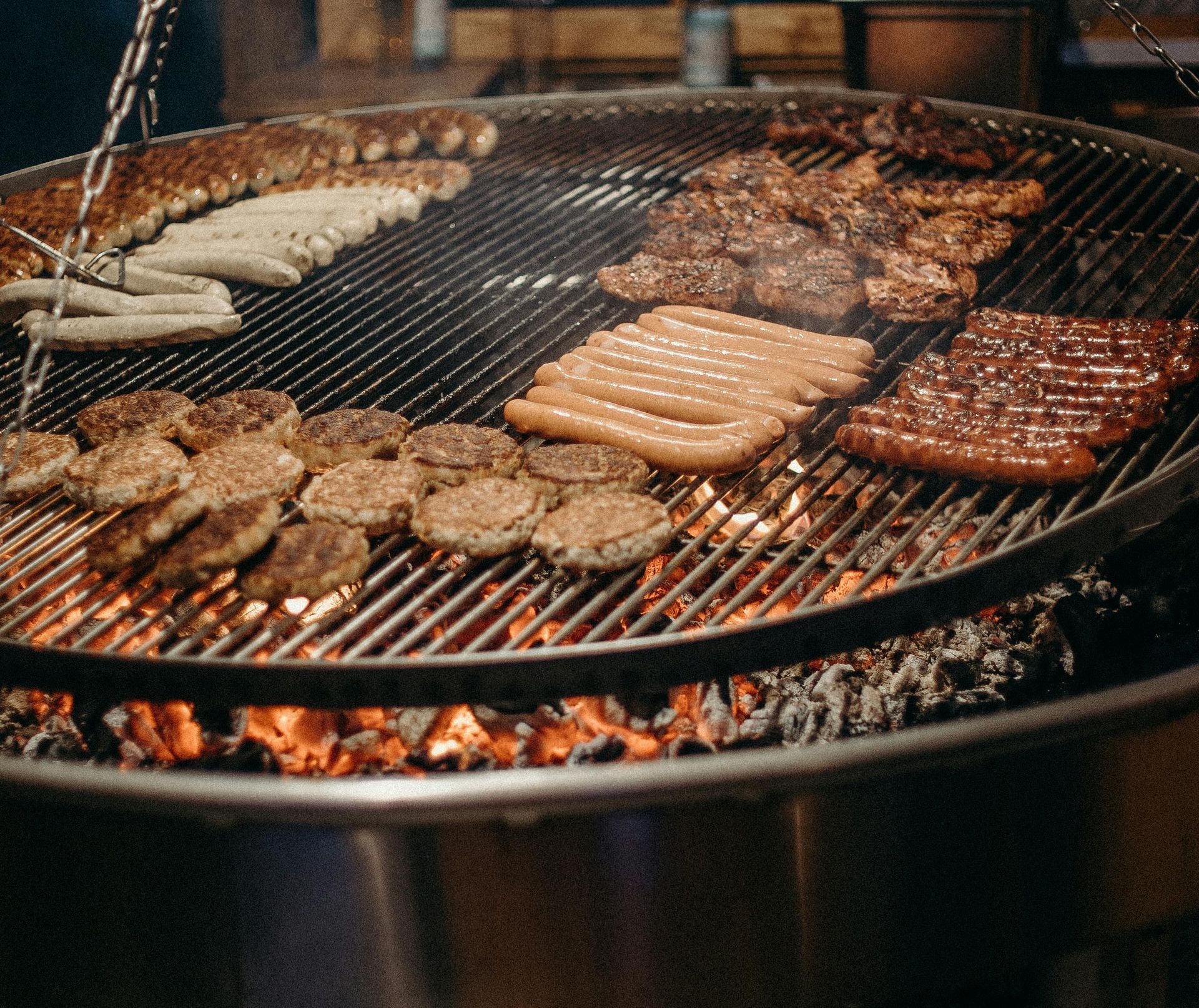 A large grill filled with meat and sausages is cooking over a fire.