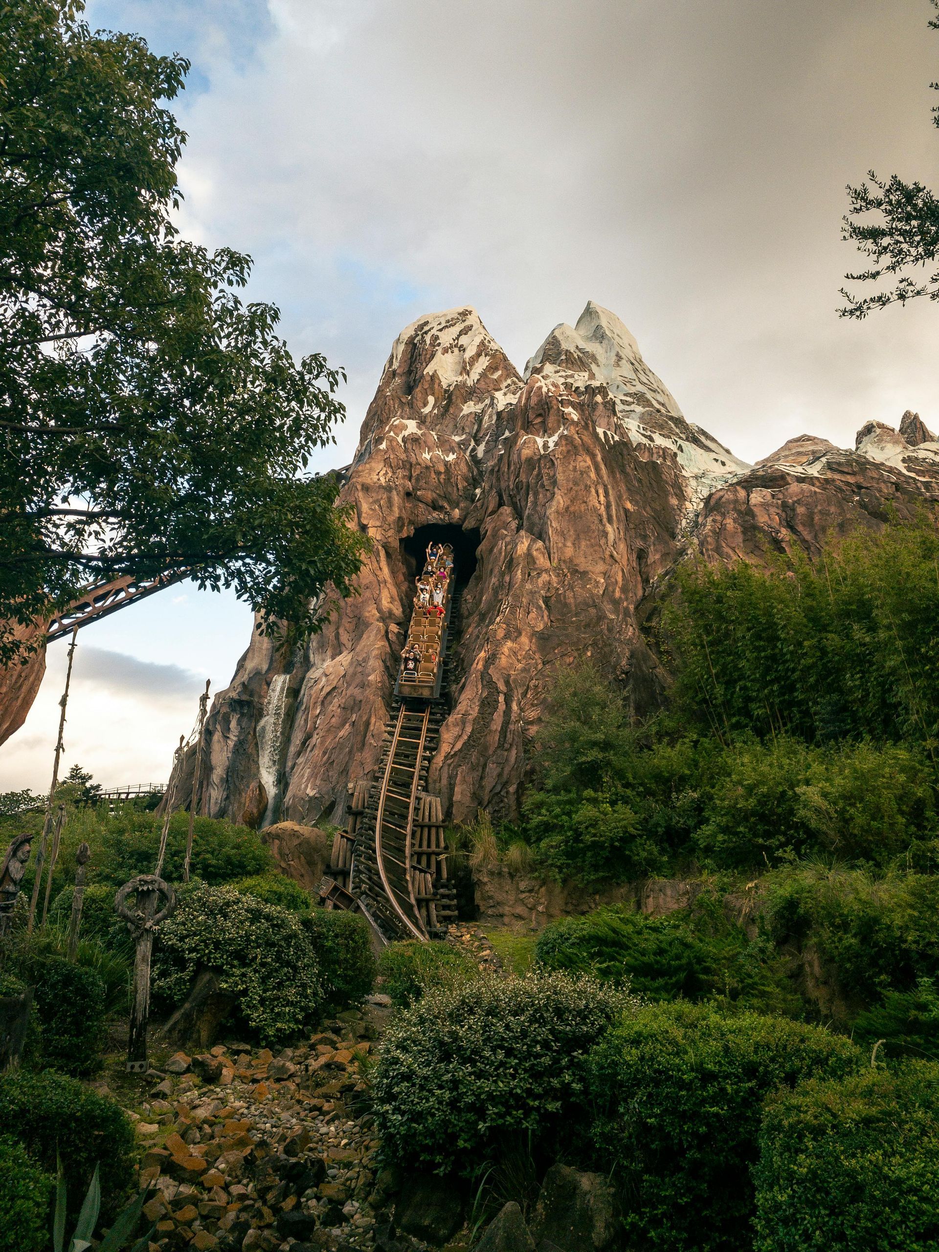 A roller coaster in front of a mountain with trees in the foreground