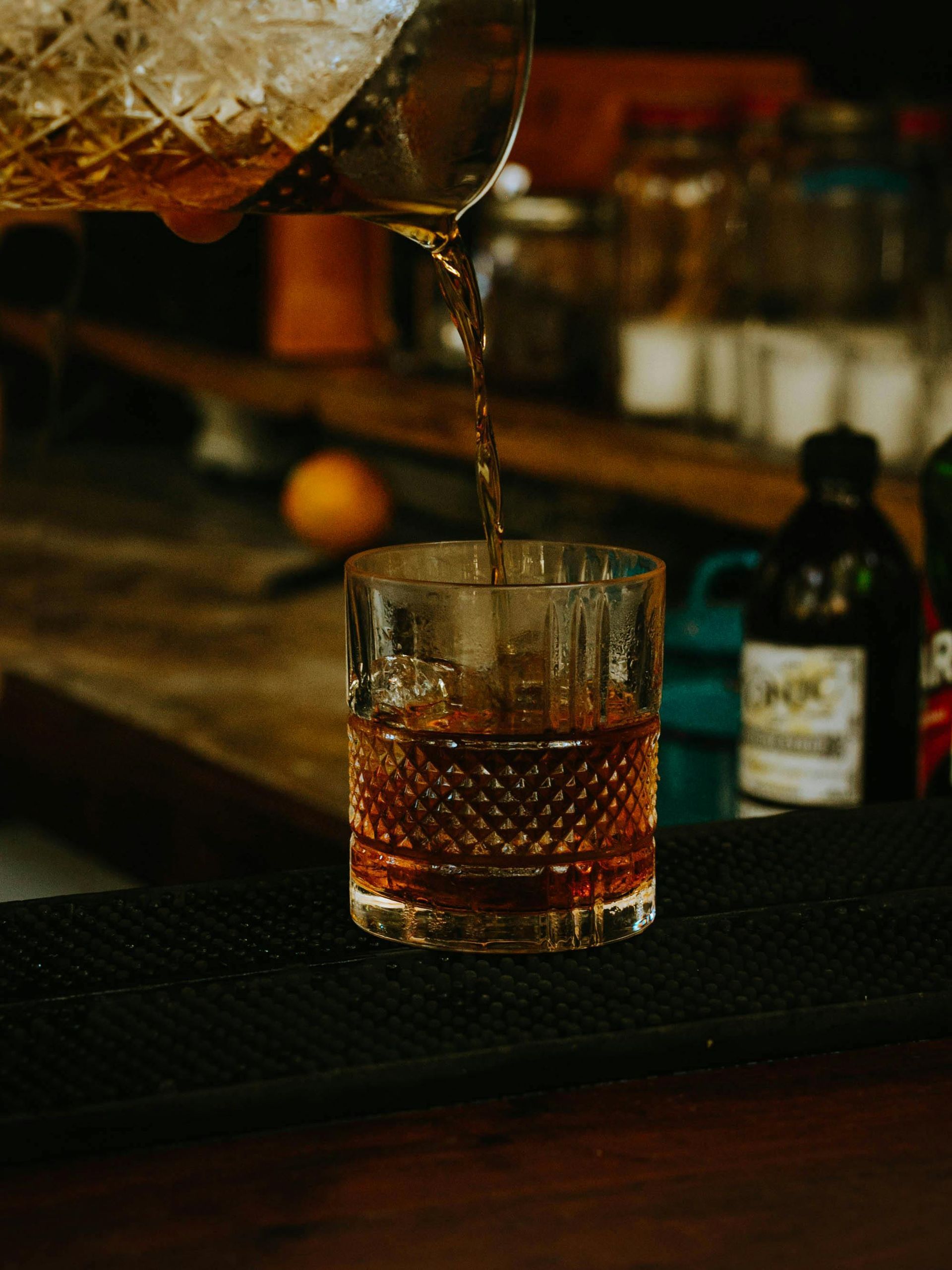 A bartender is pouring a drink into a glass on a bar.