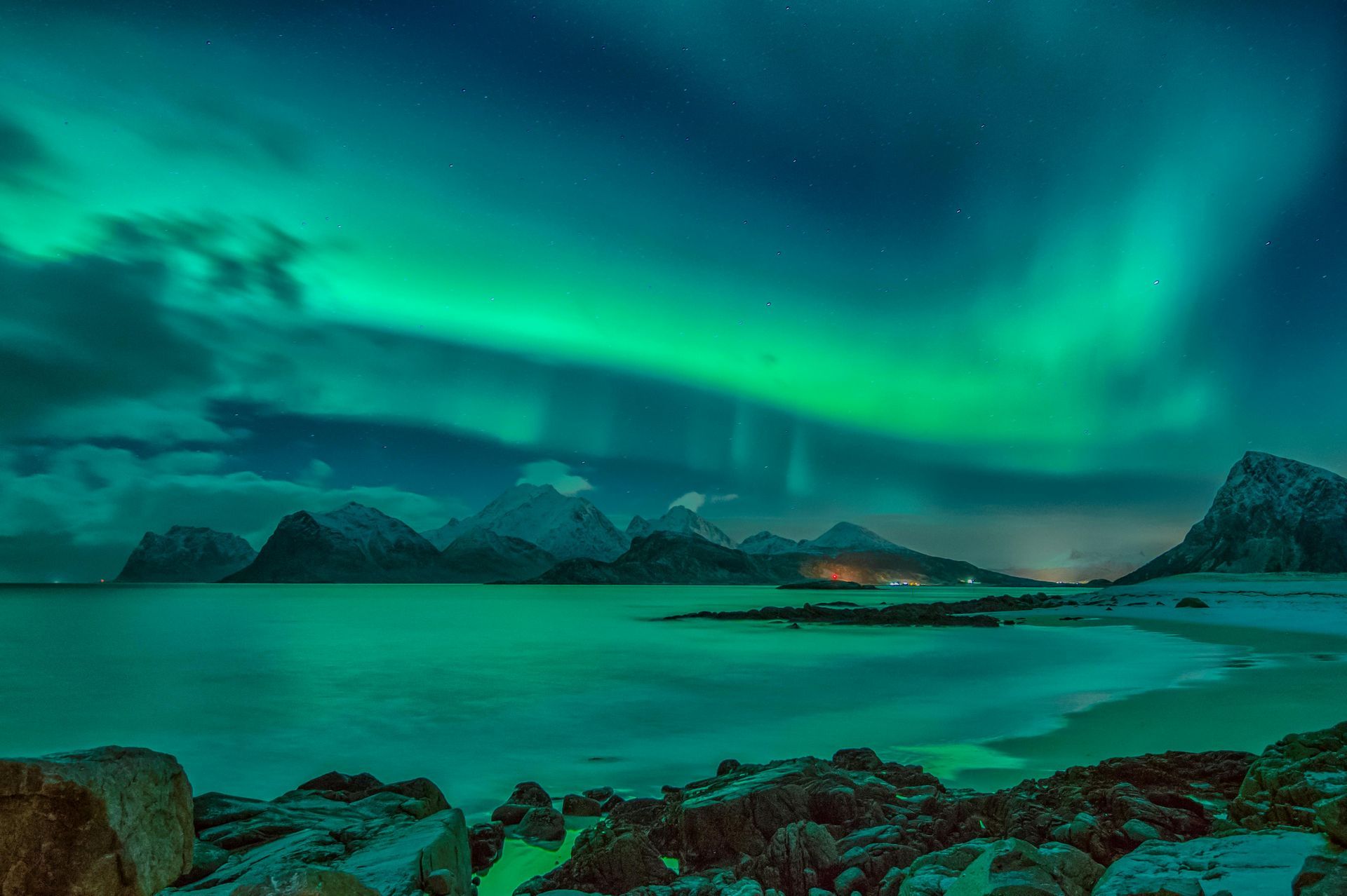 The aurora borealis is shining over the ocean and mountains.