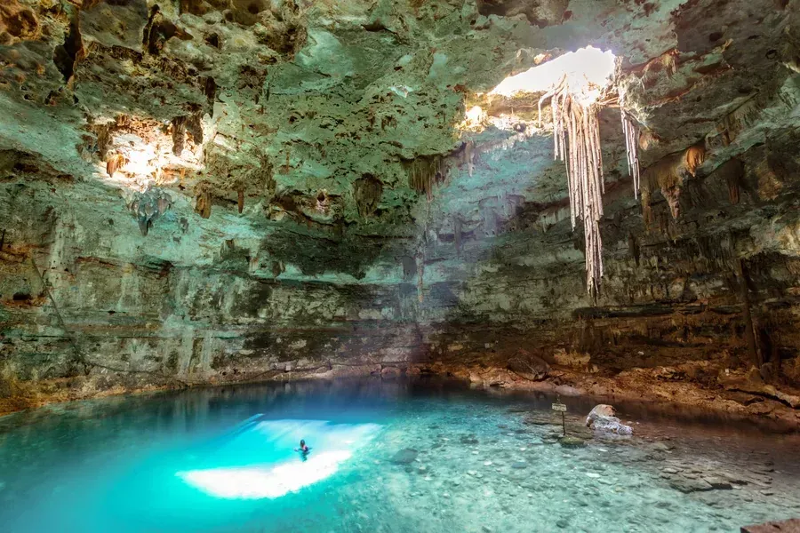 A man is swimming in a cave with a pool of water.