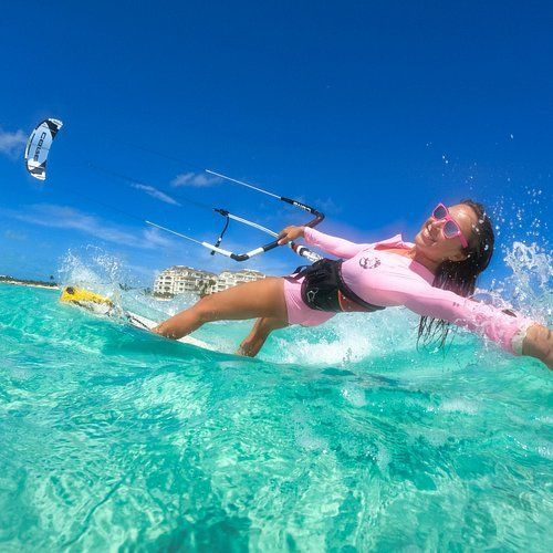 A woman is flying a kite in the ocean while riding a wave on a surfboard.