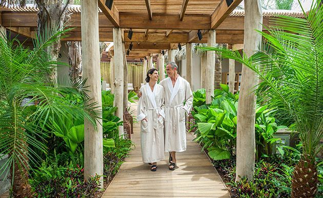 A man and a woman in bathrobes are walking down a wooden walkway.