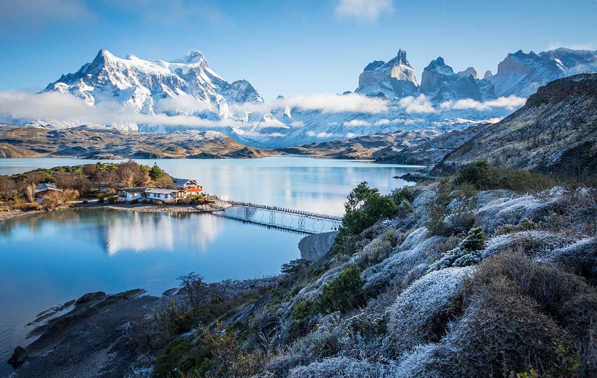 There is a bridge over a lake with mountains in the background.