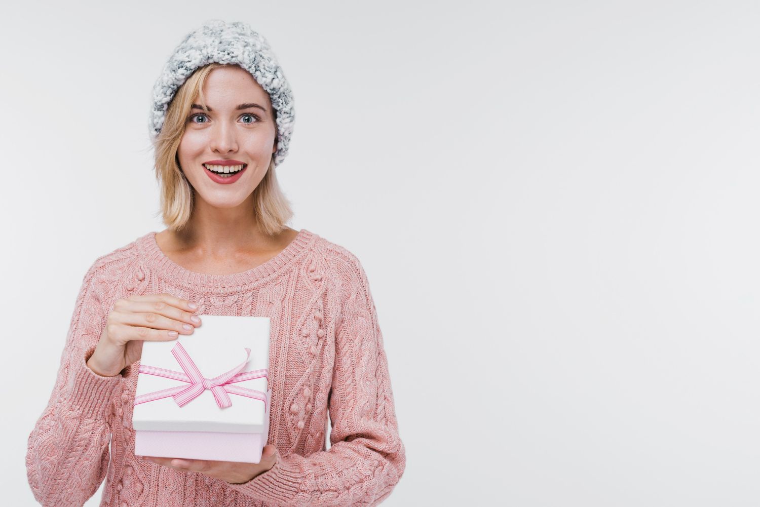 A woman in a pink sweater and hat is holding a white gift box.