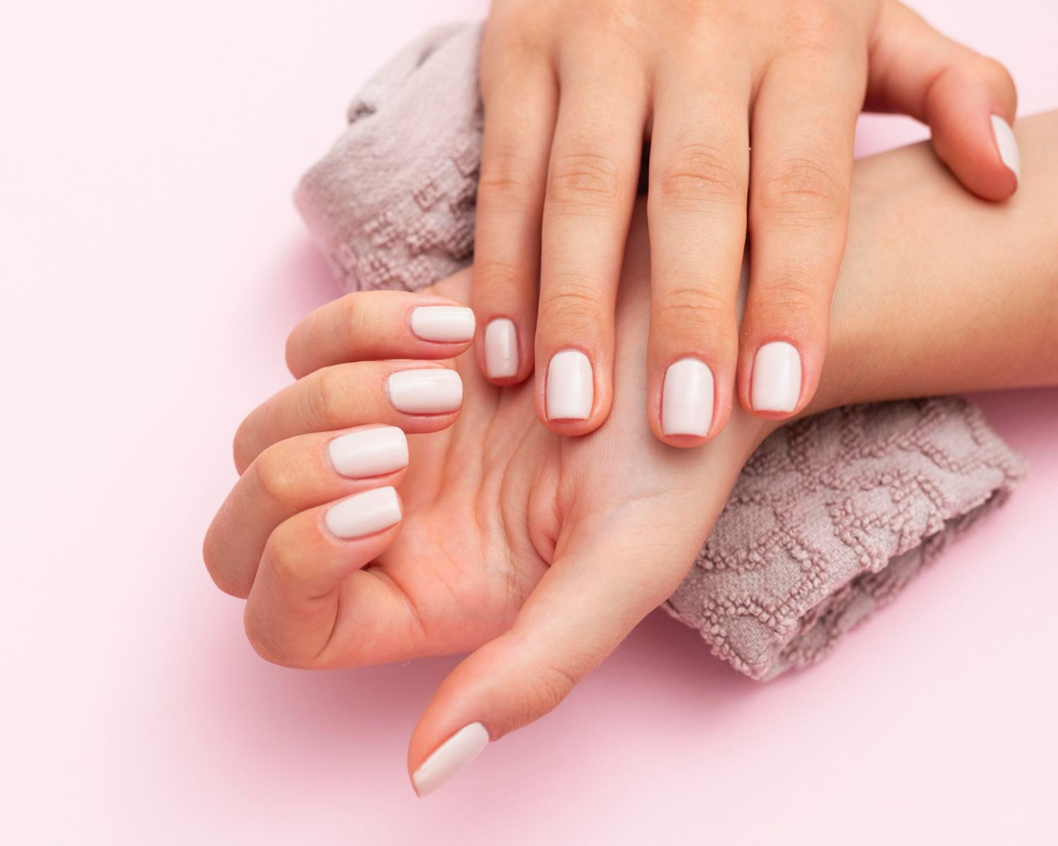 A close up of a woman 's hands with white nails on a pink background.