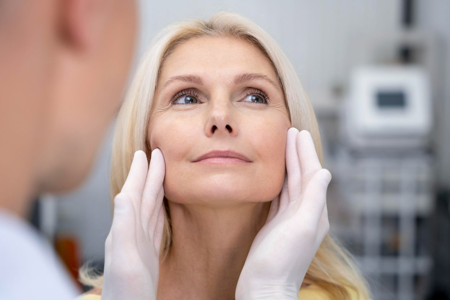 A woman is looking at her face while a doctor examines it.
