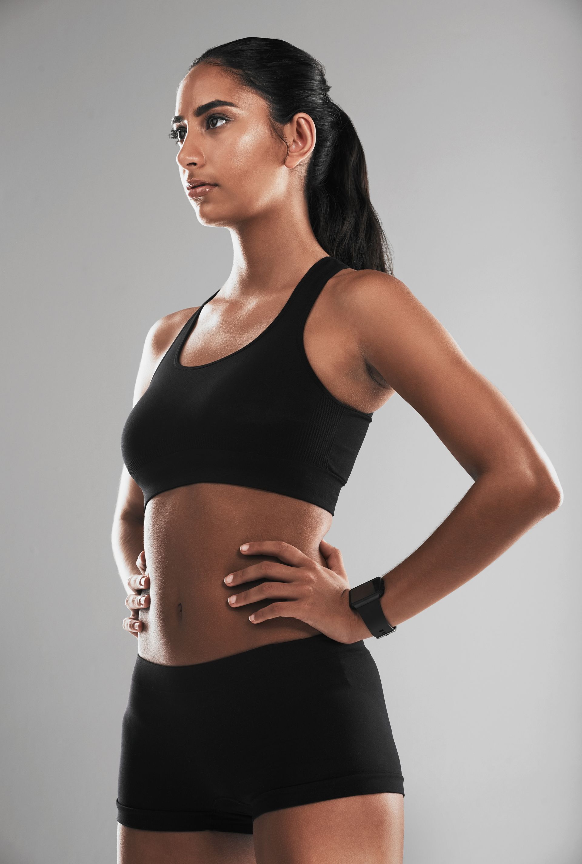 A woman in a black sports bra and shorts is standing with her hands on her hips.