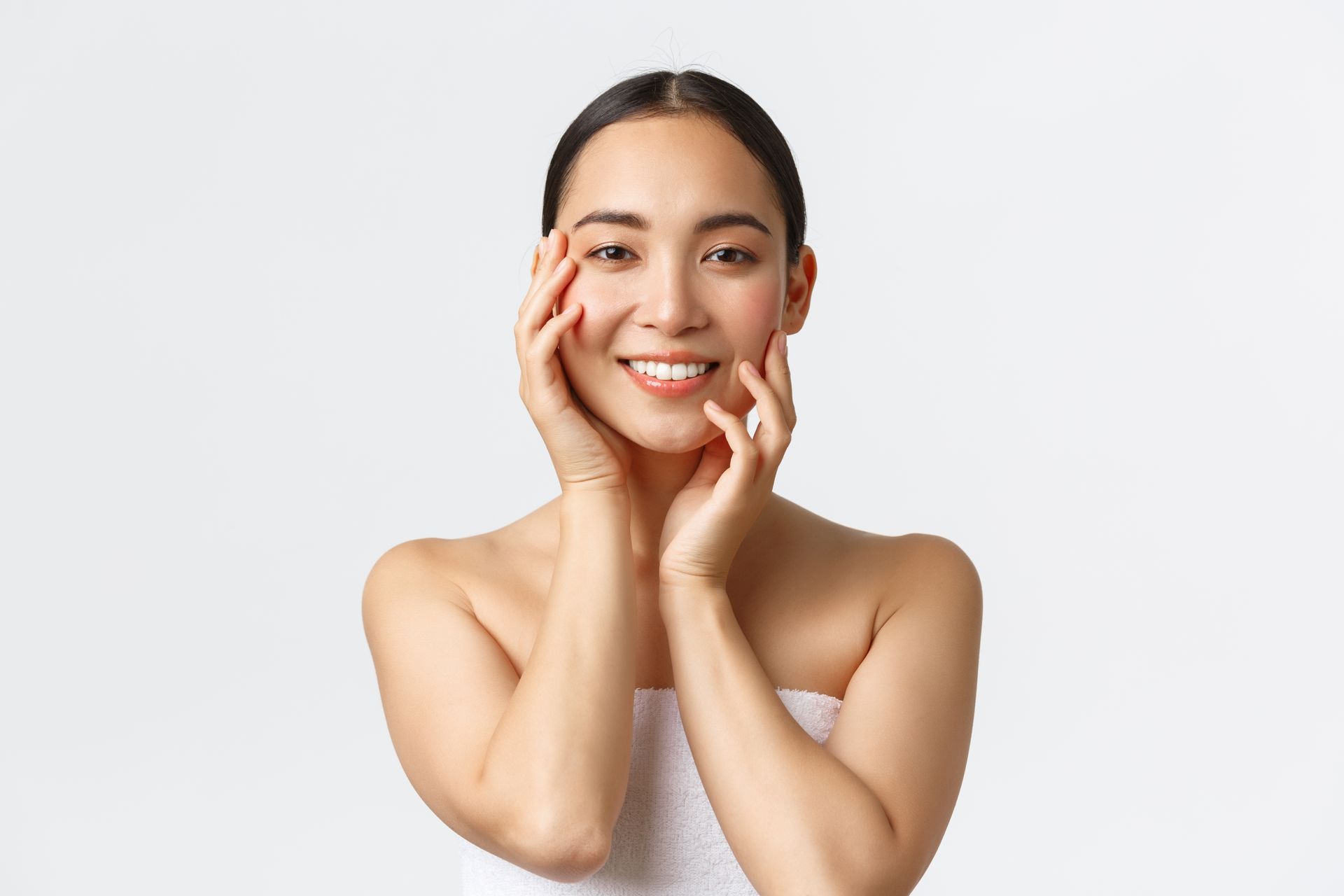 a woman wrapped in a towel is touching her face and smiling .