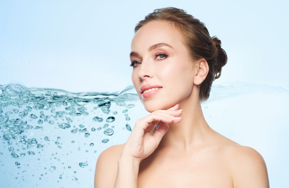 A woman is touching her face in front of a wave of water.