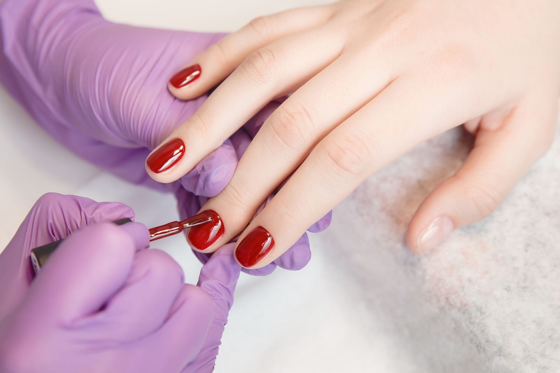 A woman is getting her nails painted by a nail artist wearing purple gloves.