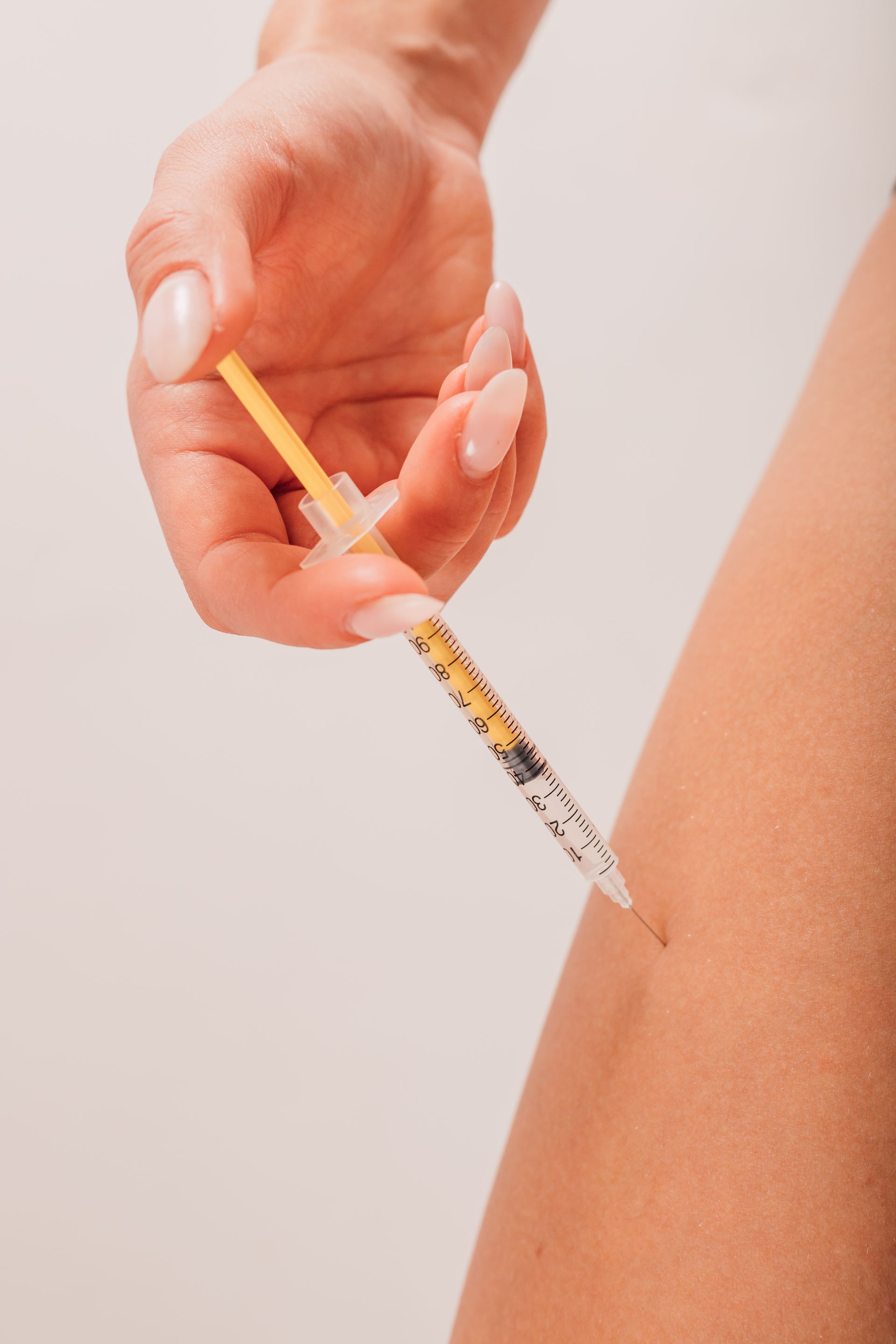 A woman is holding a syringe in her hand and injecting it into her arm.