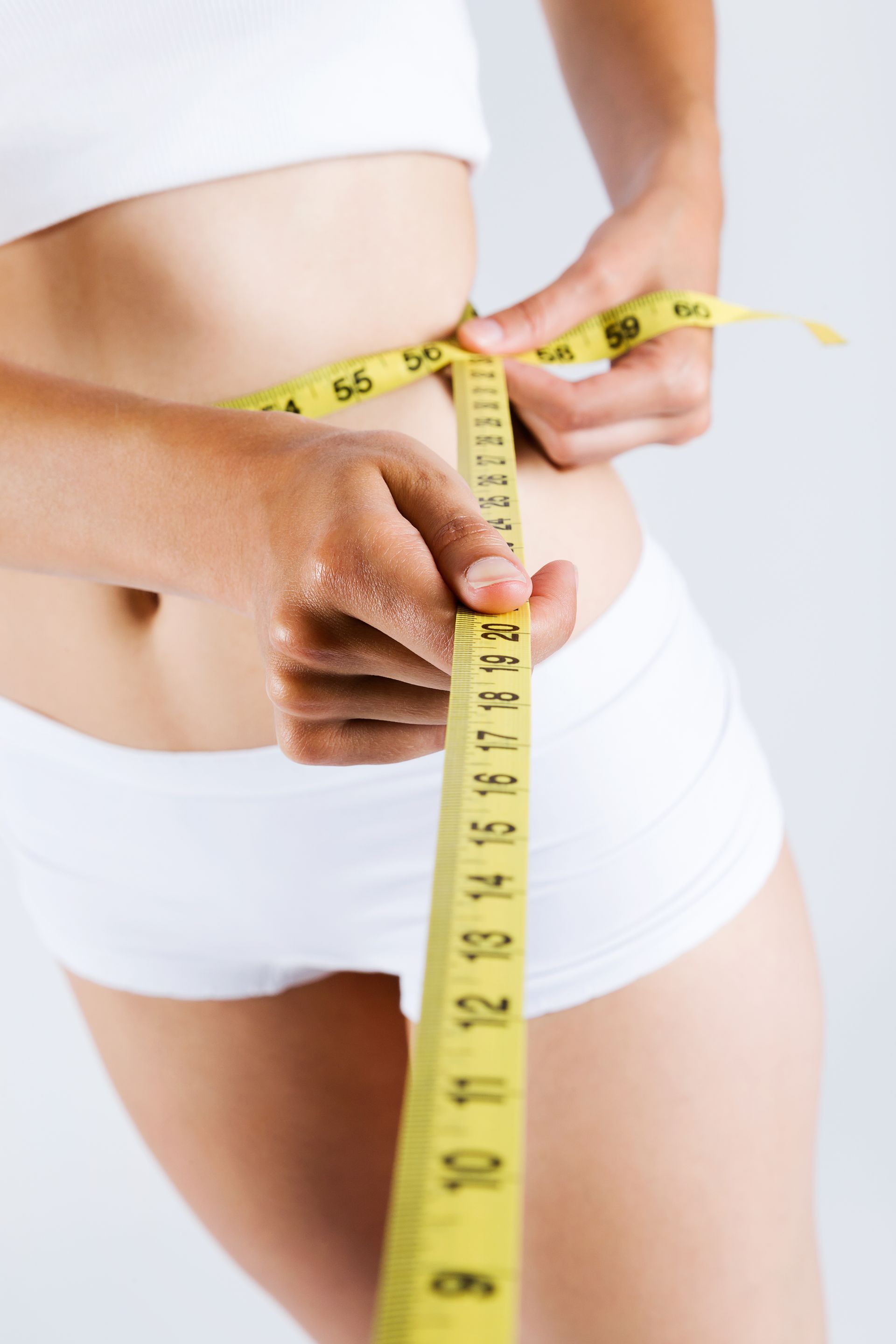 A woman is measuring her waist with a tape measure