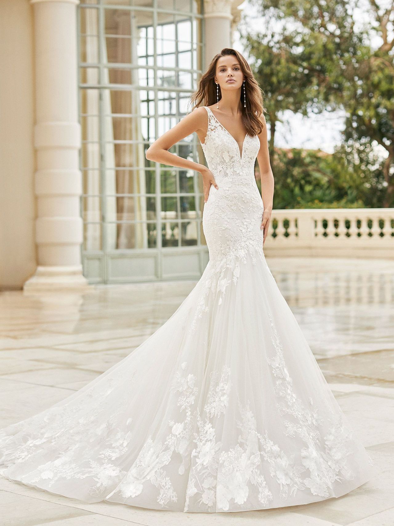 A woman in a white wedding dress and veil is standing on a balcony.