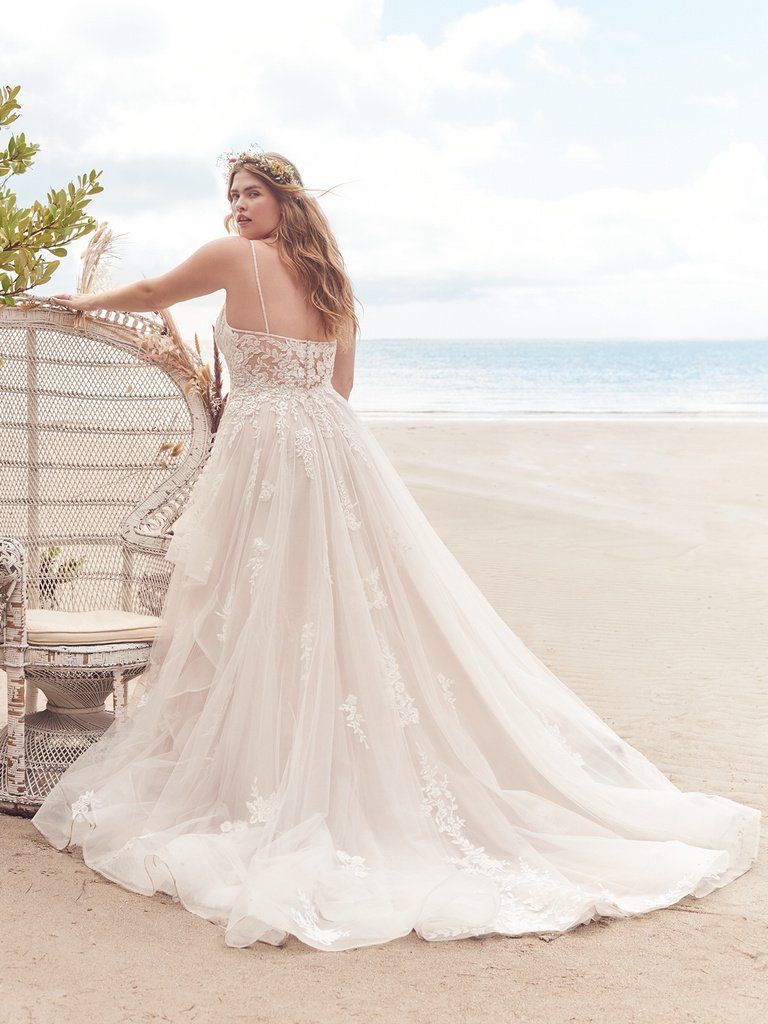 A woman in a wedding dress is standing on a beach next to a chair.
