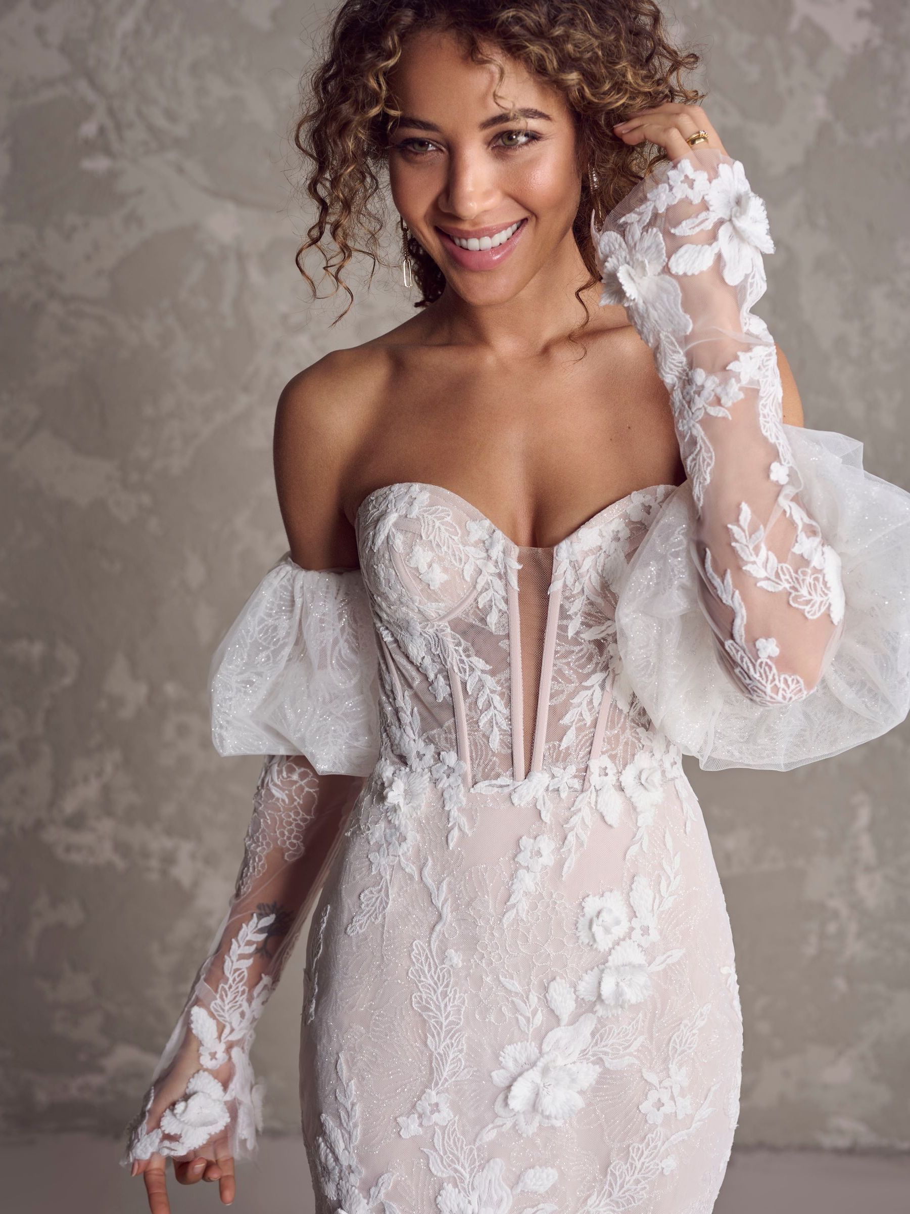A woman is wearing a wedding dress and gloves and smiling.