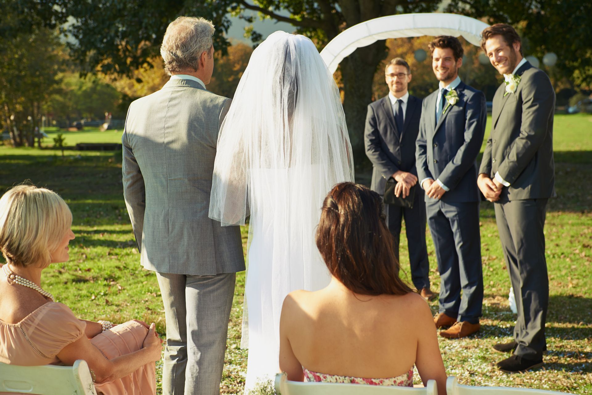 A bride in a wedding dress is sitting on the ground holding a bouquet of flowers.