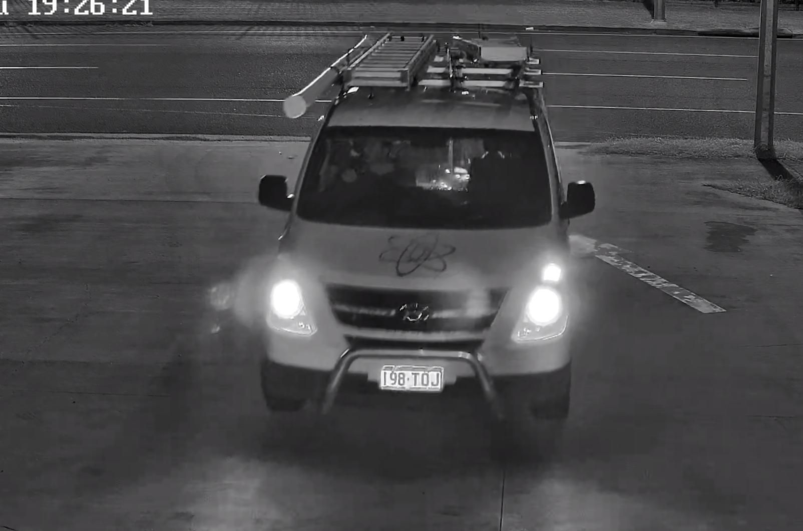 A Grayscale Surveillance Photo Of A Utility Van Driving On A Wet Road At Night. The Van's Headlights Are On, And Its License Plate Is Visible — Advanced Alarms Mackay Pty Ltd In South Mackay, QLD