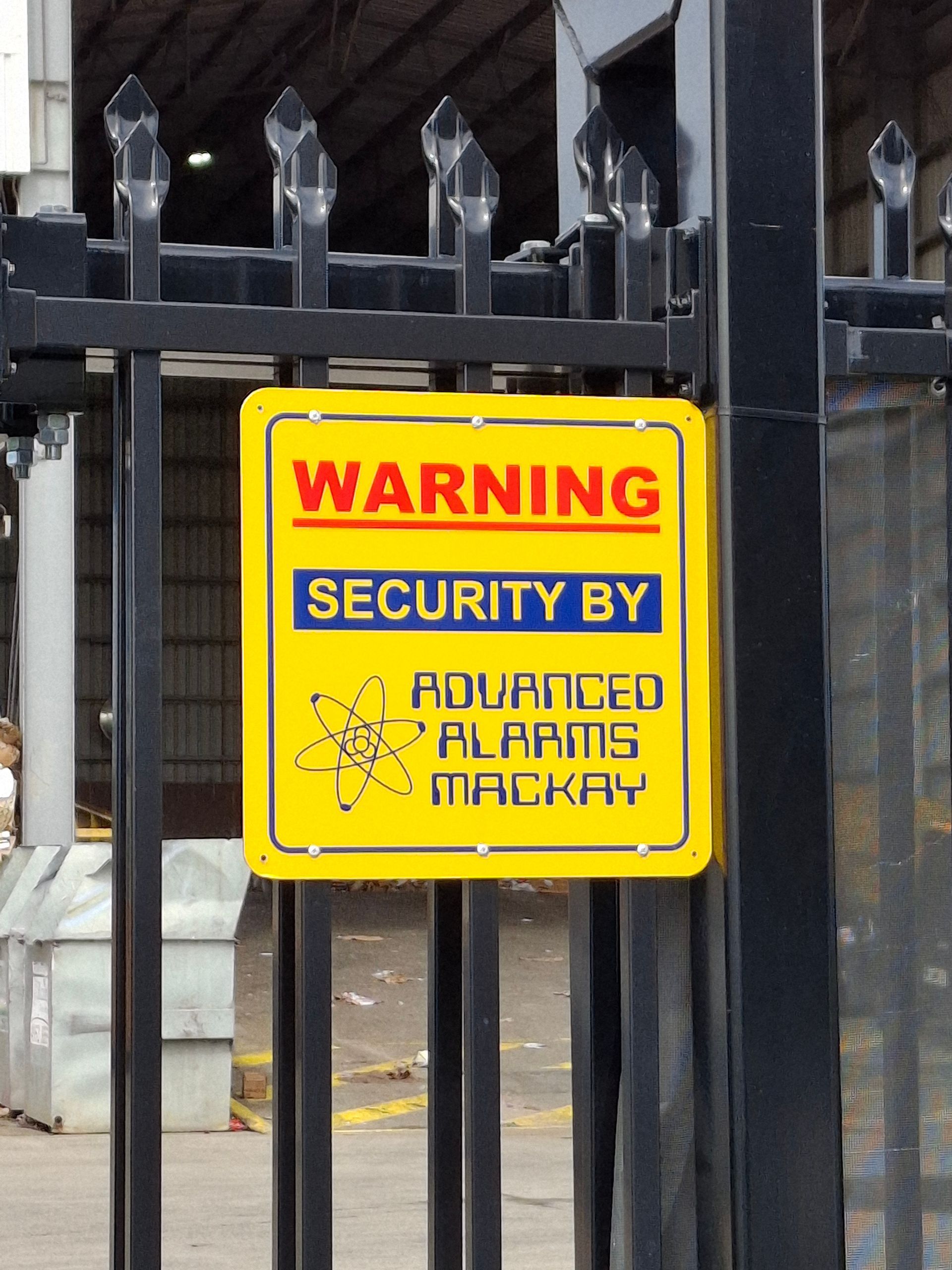 Yellow warning sign on a black metal gate: