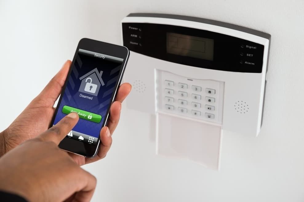 Person Unlocking A Home Security System Via A Smartphone App, Alongside A Wall-mounted Keypad — Advanced Alarms Mackay Pty Ltd In South Mackay, QLD