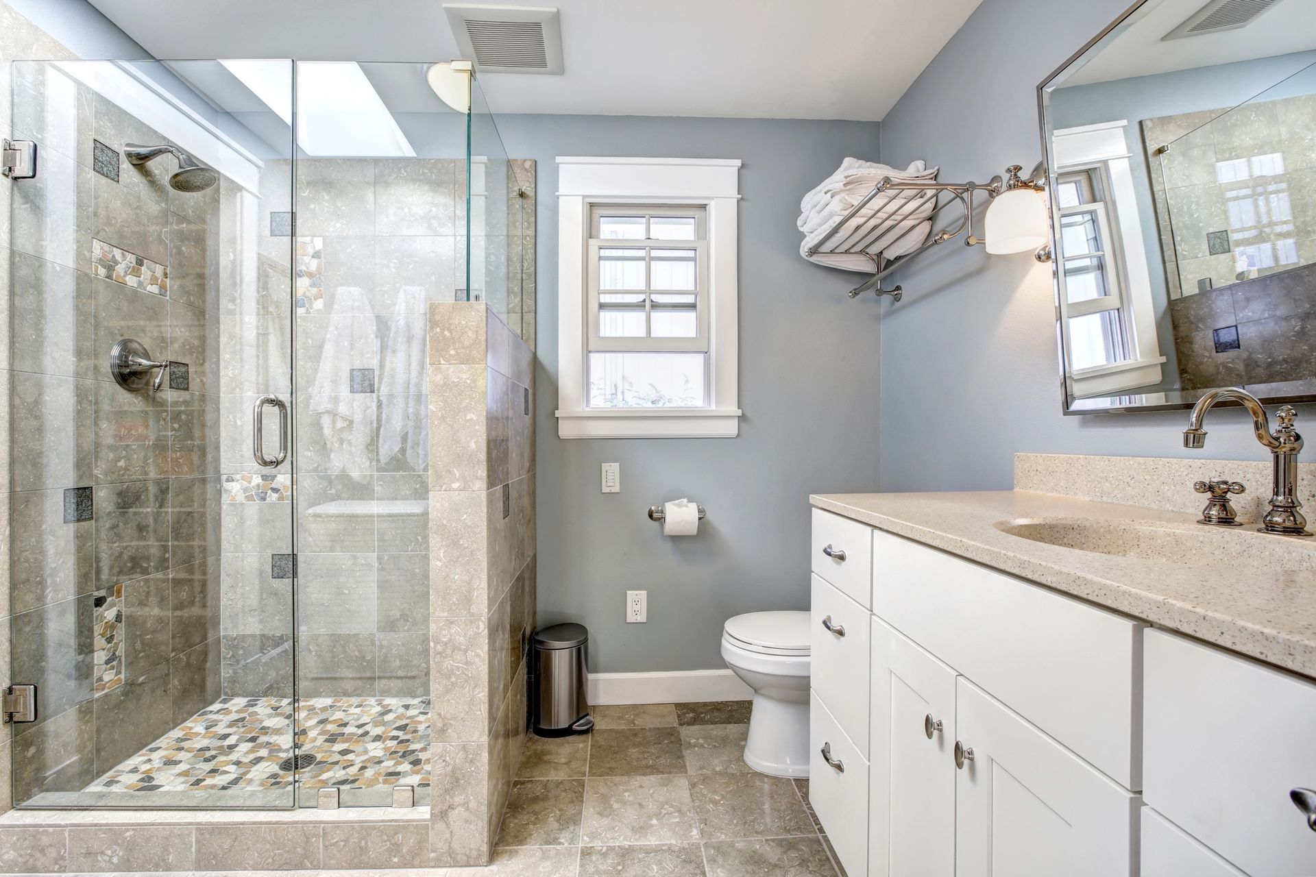 Bright bathroom with glass walk-in shower, white vanity, toilet, and window on gray walls