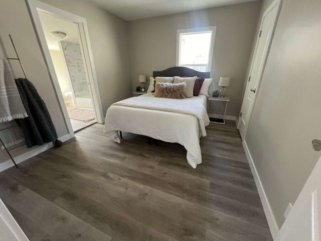 Bright bedroom with a made bed, gray walls, wood flooring, and a window between two bedside tables.