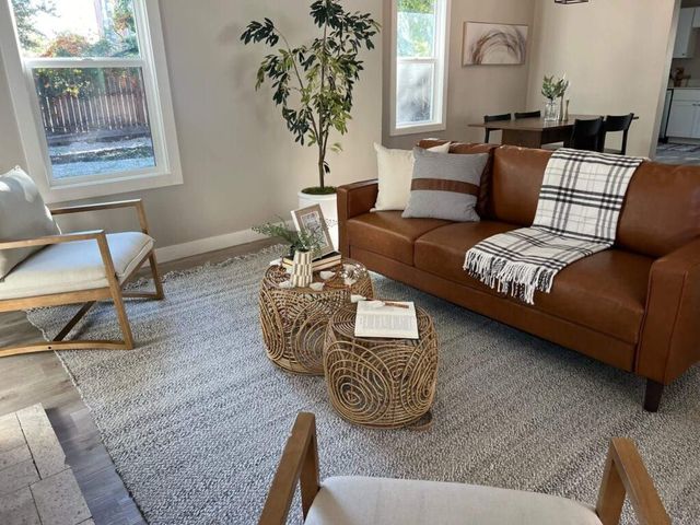 Bright living room with a brown sofa, woven coffee tables, rug, plant, and natural light from windows