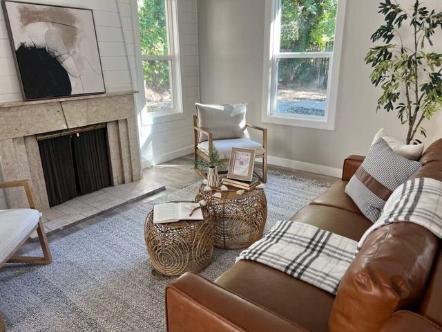 Bright living room with a brown leather sofa, white armchair, woven baskets, and a fireplace.