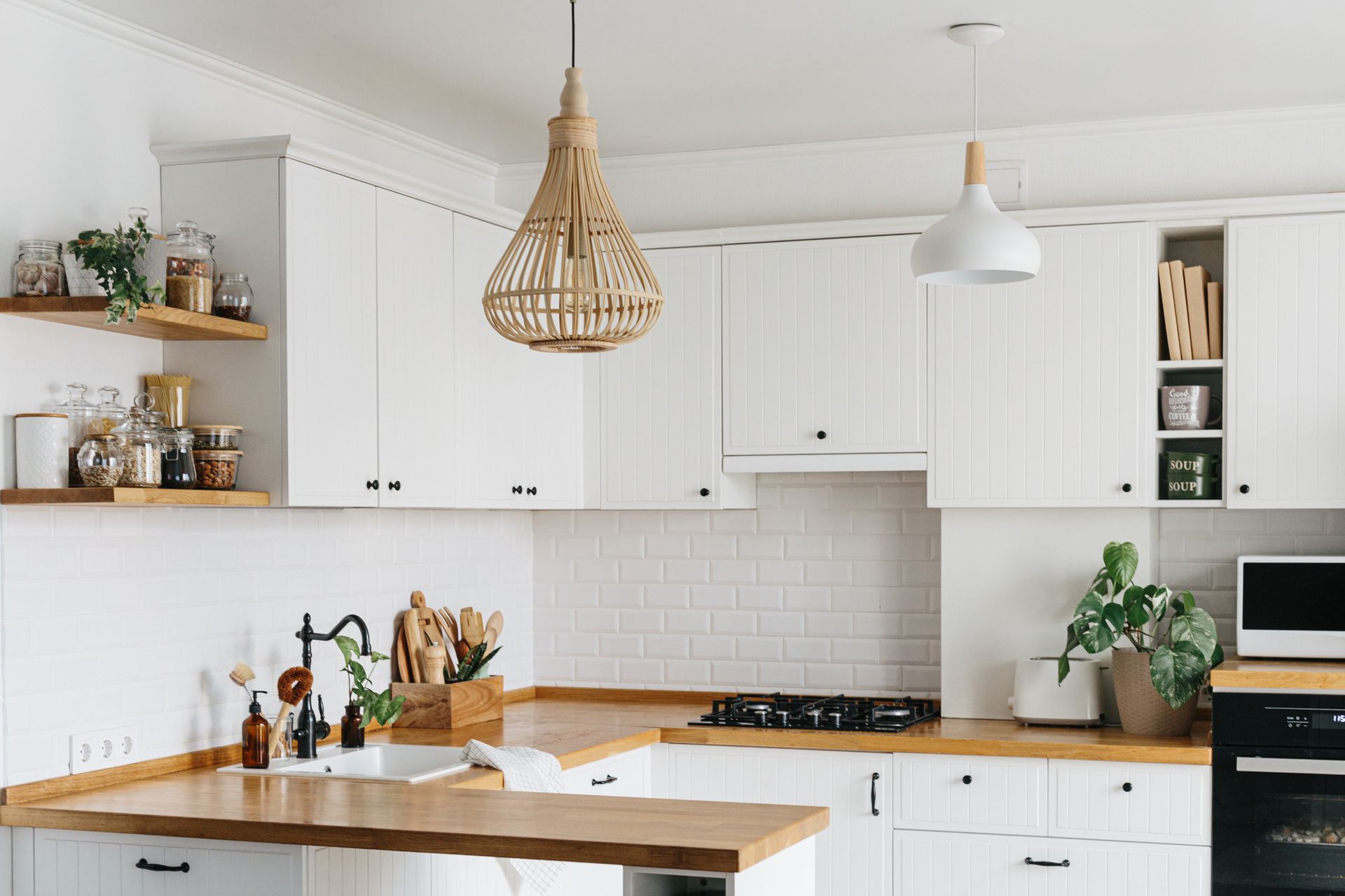 White kitchen with wooden countertops, white cabinets, and woven pendant light.