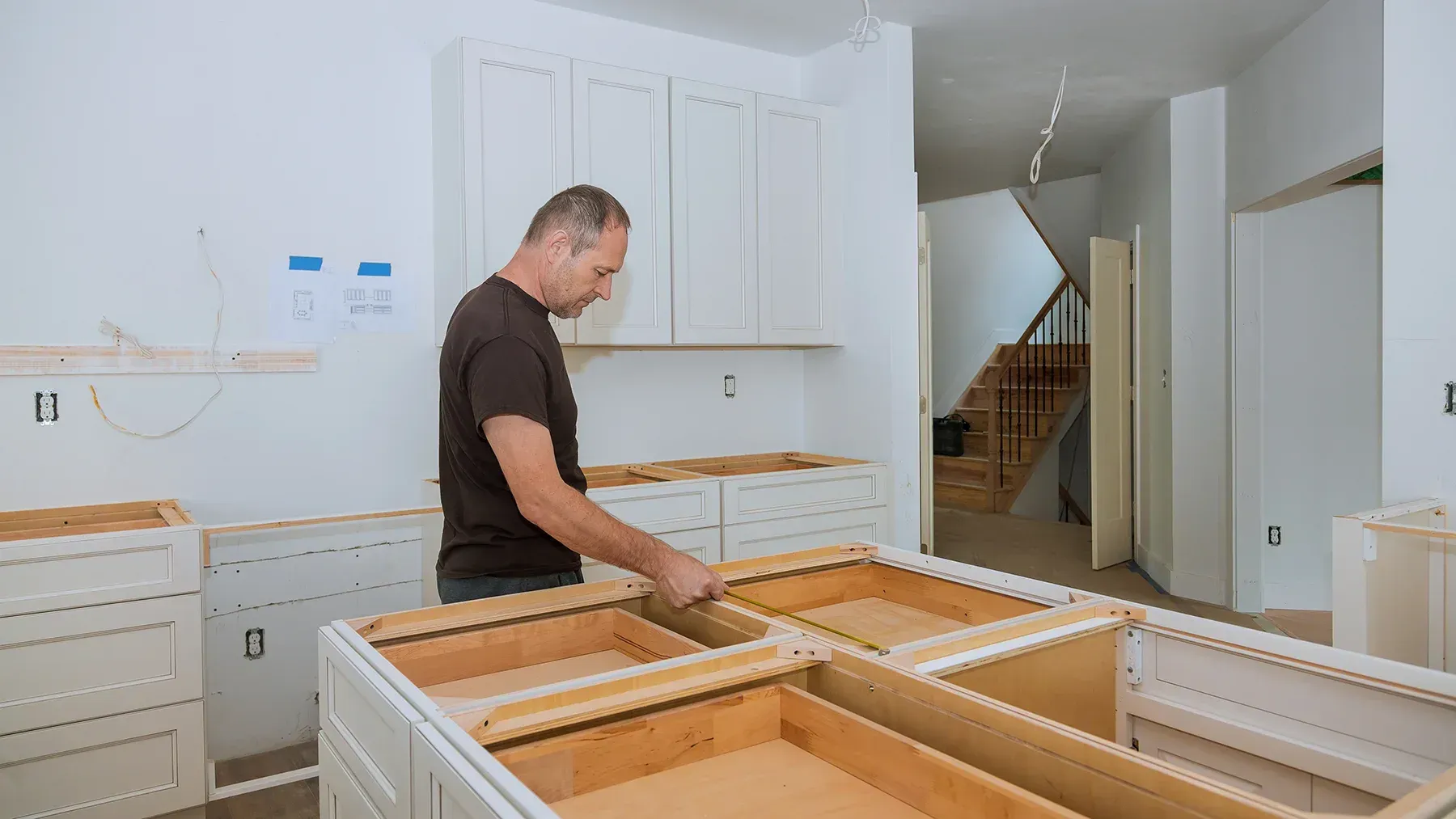 A man measures space in a kitchen during cabinet installation