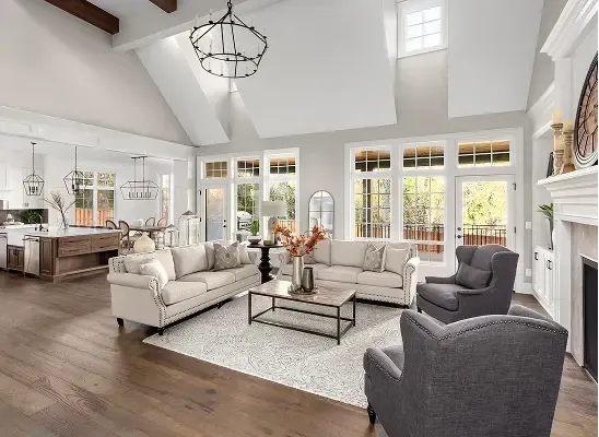 Bright open living room with white sofas, gray chairs, fireplace, and large windows.