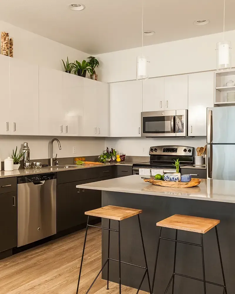 Modern kitchen with white cabinets, stainless steel appliances, black countertops, and two wooden stools at an island