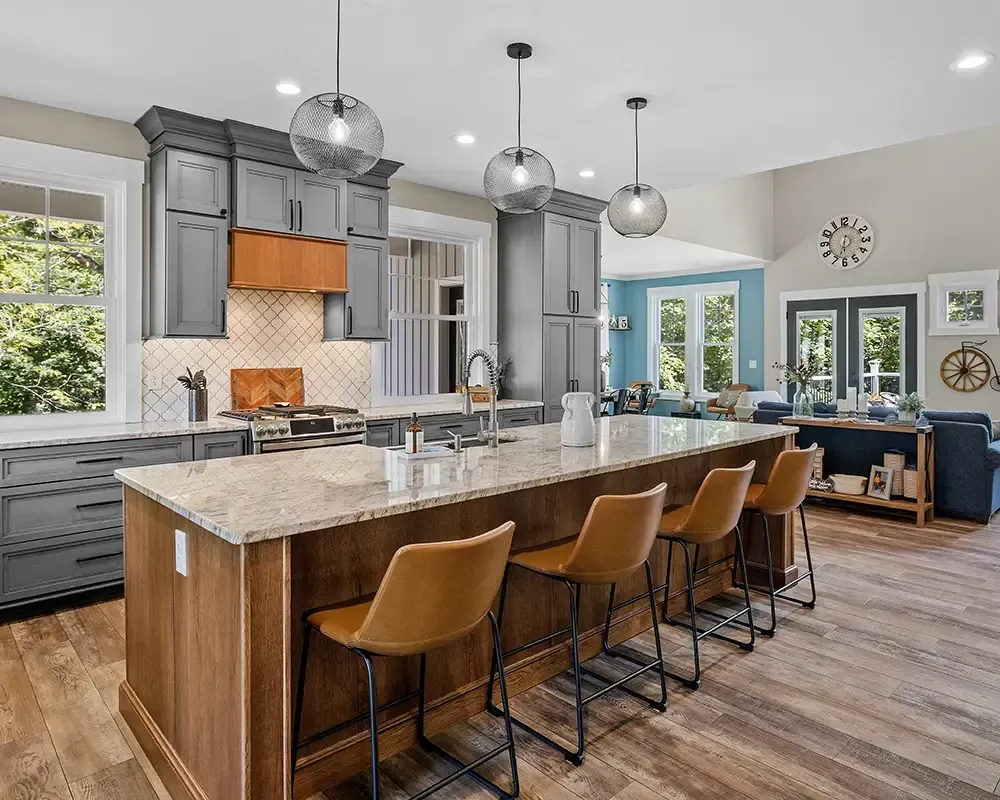 Modern kitchen with marble island, wood stools, gray cabinets, and blue seating area in the background